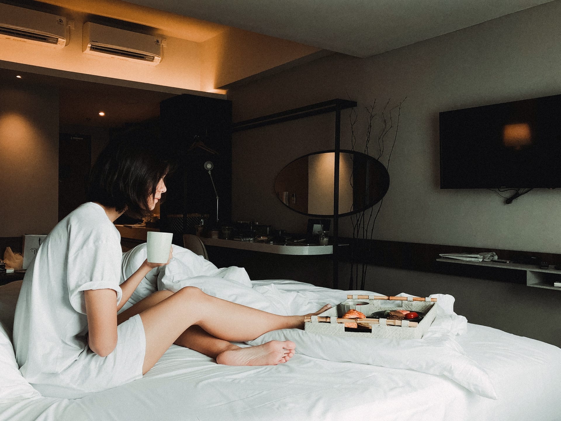 Guest having coffee in bed beside a breakfast tray in the warm evening light of her room