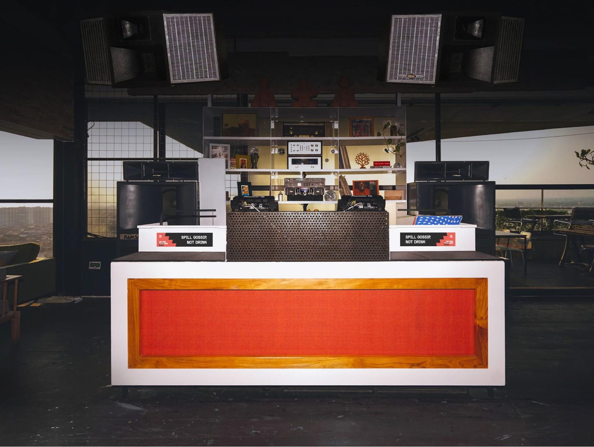 White-and-orange DJ booth with twin decks flanked by RAMSA speakers at 18+ Music Bar