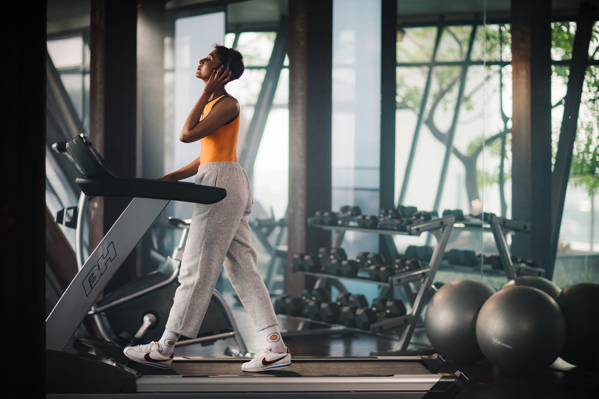 Guest in headphones walking a treadmill past dumbbell racks and exercise balls in the gym