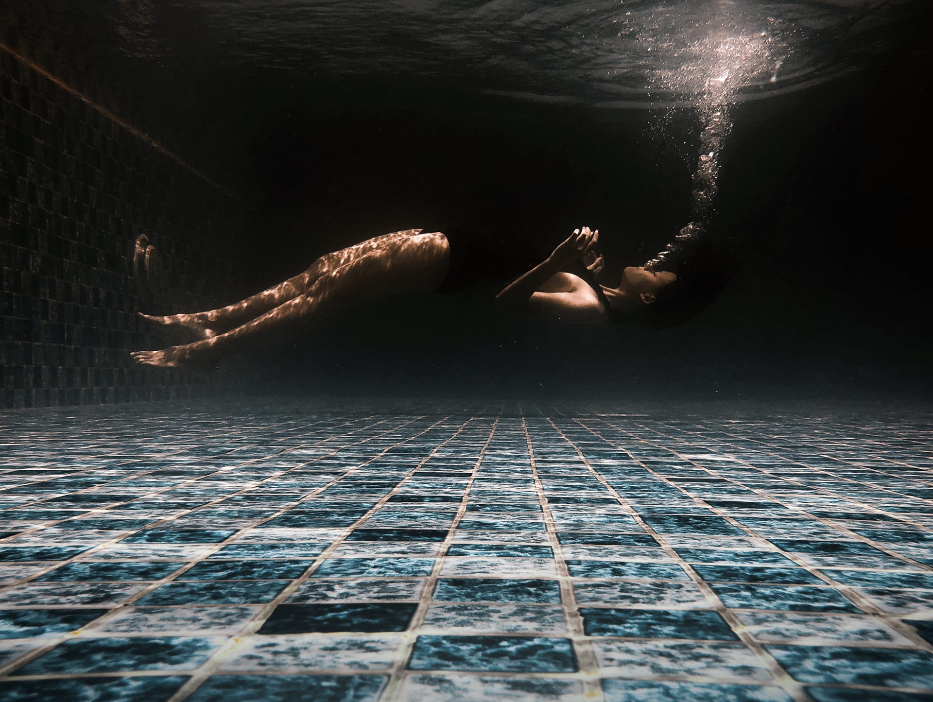 Swimmer drifting underwater above the blue-tiled floor of the sky-pool