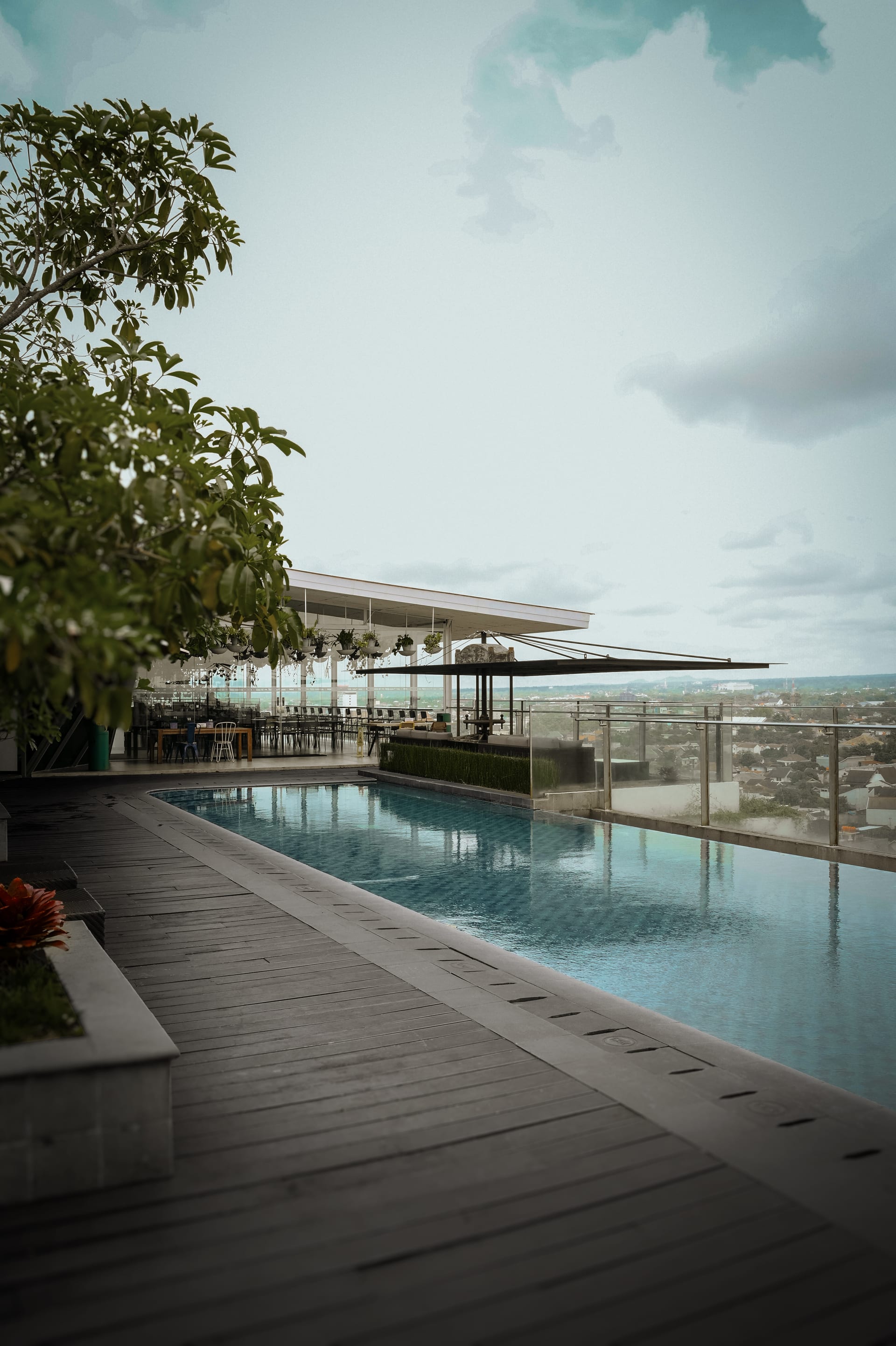 Timber deck running beside the sky-pool, with the plant-hung rooftop pavilion and Jogja spread below