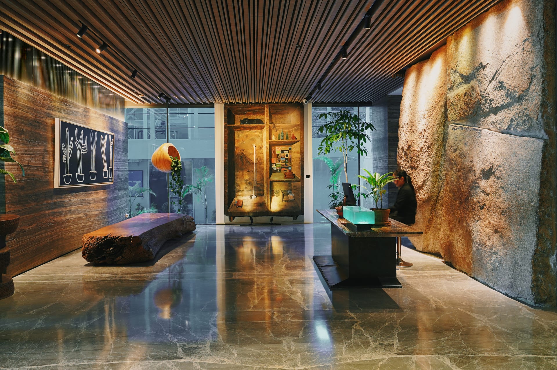Solid timber log bench beneath a cactus painting on the travertine wall of the PULANG ke UTTARA lobby