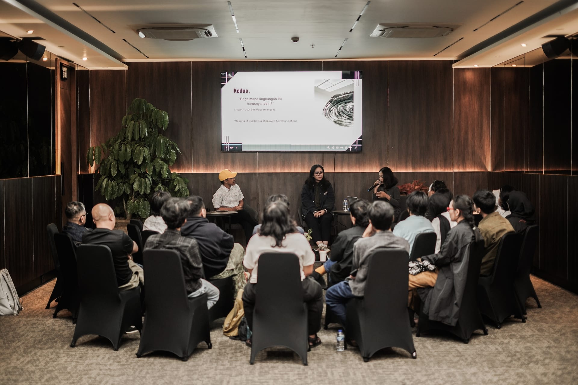 Audience circled around three panel speakers beneath the screen in the Omong-Omong meeting room