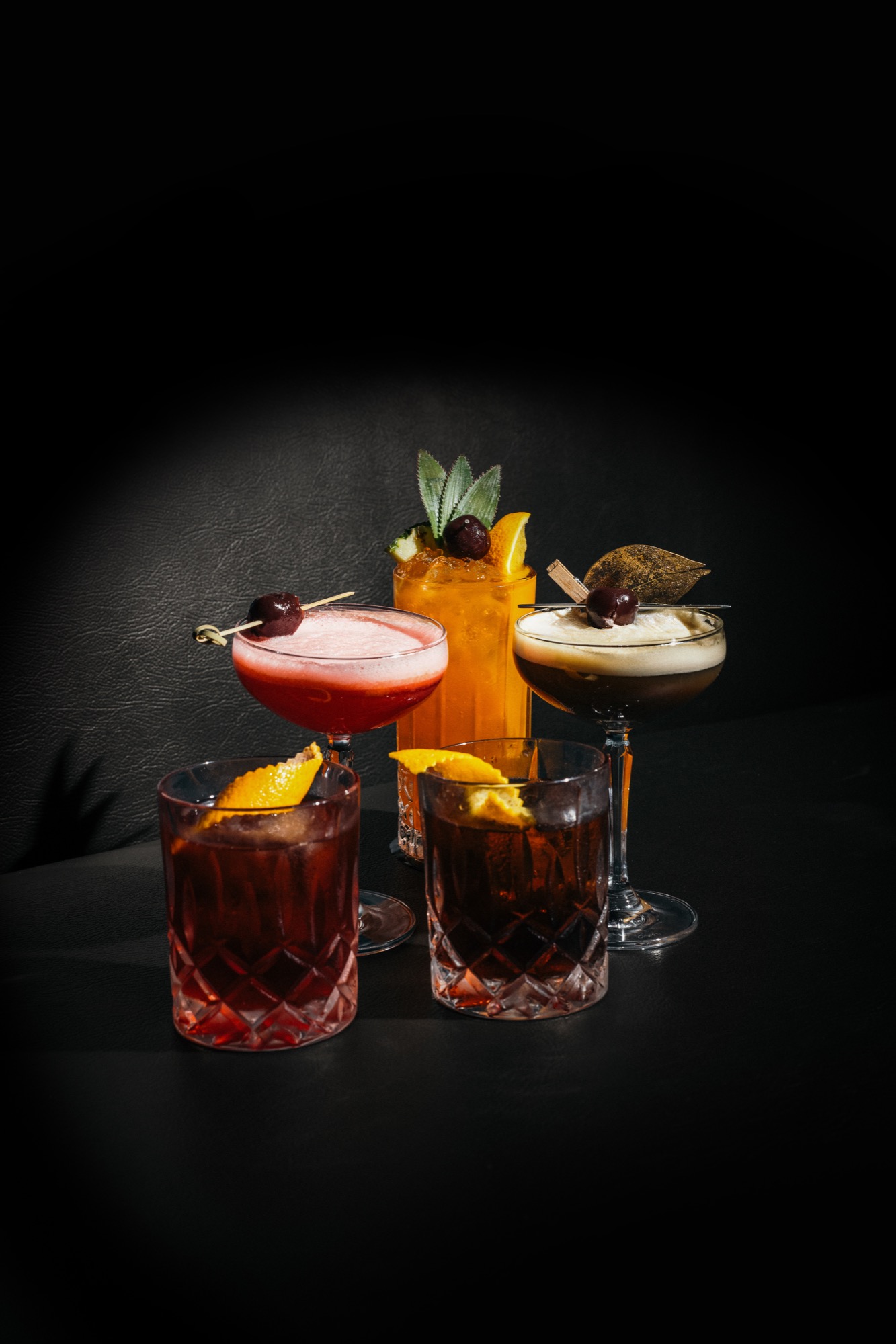 Five garnished cocktails in cut glassware against the dark backdrop of 18+ Music Bar